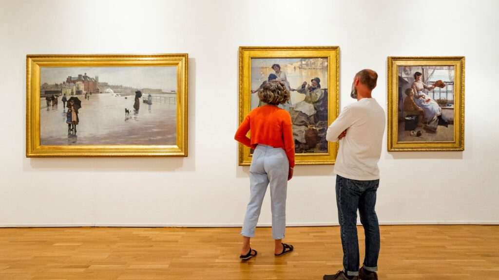 Visitors looking at a painting at Penlee House Gallery & Museum