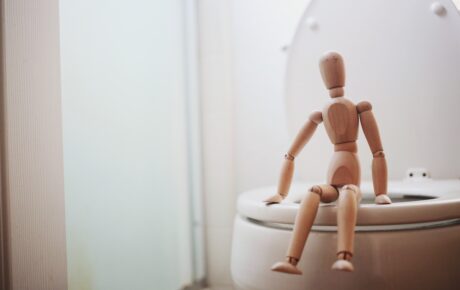 Mini wooden manikin sitting on a toilet seat