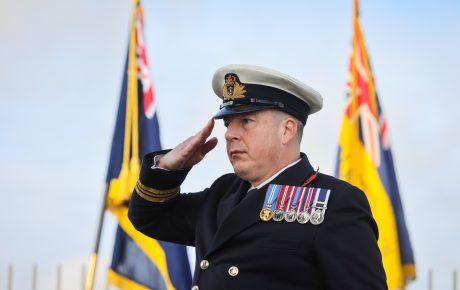 Naval Commander in full uniform saluting with standards in the background