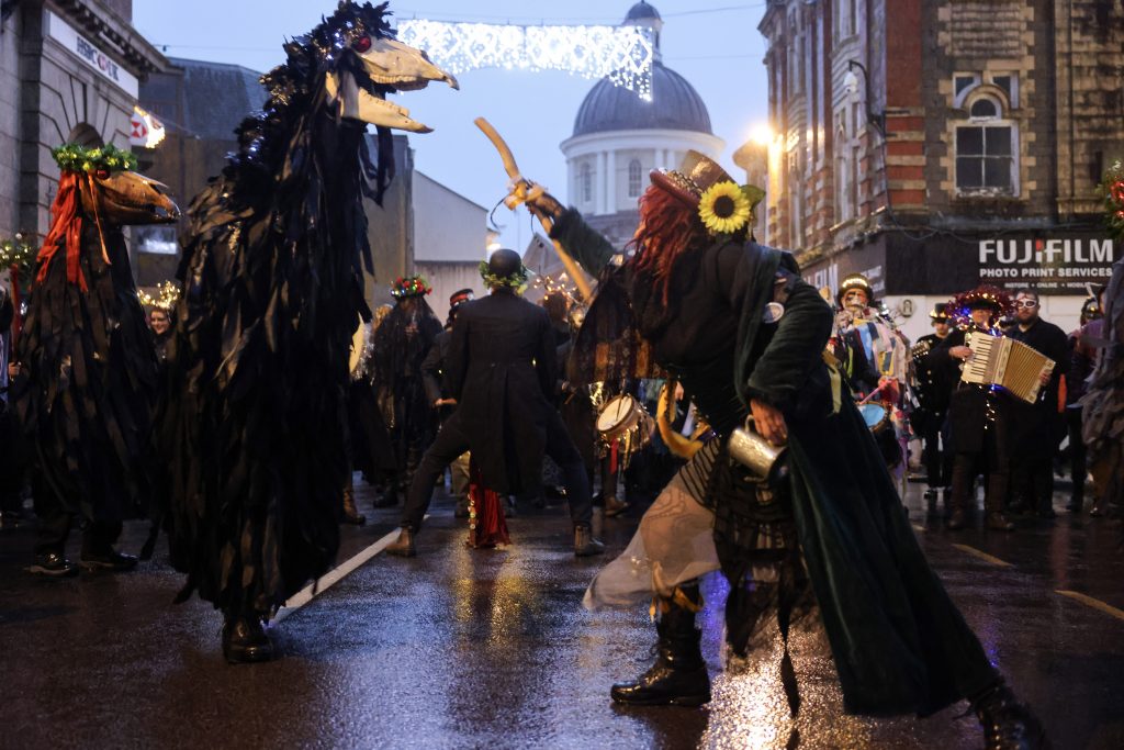A Montol Oss being teased in the Greenmarket with the Market House and Christmas Lights in the background